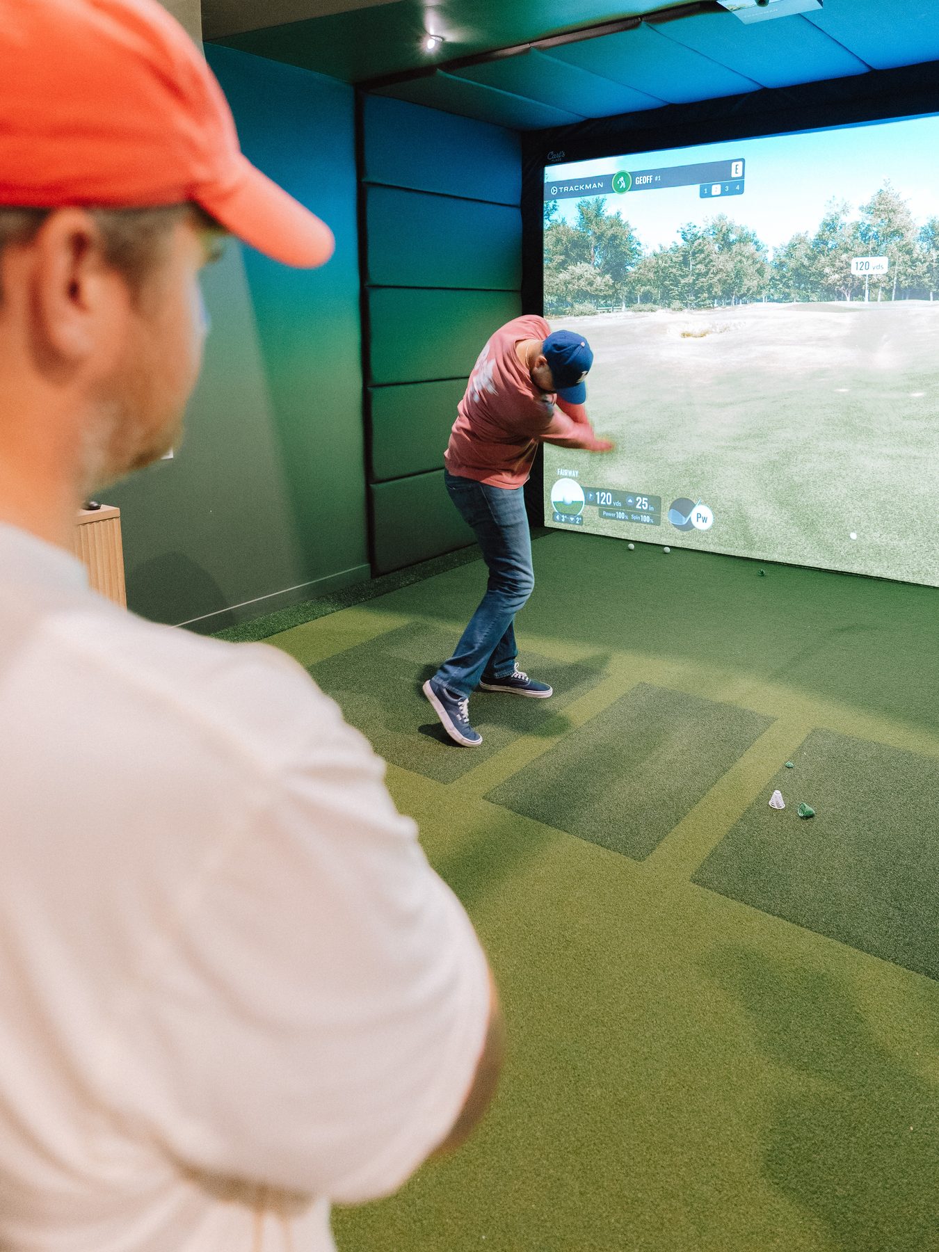Two golfers watching a shot on the TrackMan screen